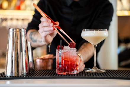 Barman ajustant une paille dans un cocktail rouge sur glace, verre à coupe en arrière-plan, bar Honfleur, restaurant L'Assiette Normande