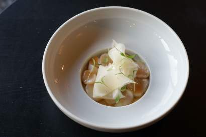 Velouté clair avec copeaux de fromage et herbes fraîches dans un bol blanc, spécialité normande servie en entrée du restaurant L'Assiette Normande à Honfleur