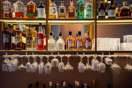 Étagères de bar garnies de spiritueux et rangées de verres suspendus sous éclairage doré, bar Honfleur centre ville, restaurant L'Assiette Normande