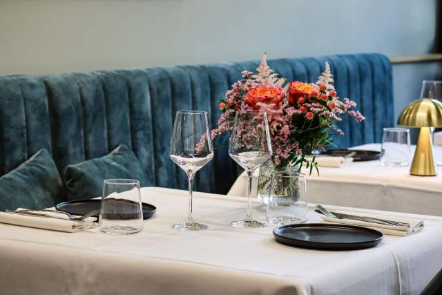 Table dressée avec bouquet de fleurs orangées, verres à pied et banquette velours bleue, bistronomique L'Assiette Normande à Honfleur