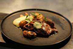 Pièce de viande poêlée avec champignons et jus réduit sur assiette noire, restaurant L'Assiette Normande fait maison à Honfleur