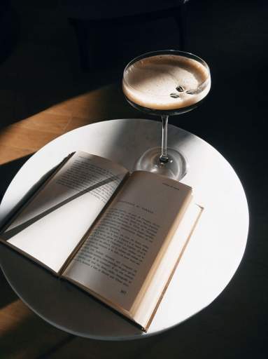 Verre à cocktail et livre ouvert posés sur une table ronde blanche, café Honfleur en ambiance lecture due restaurant L'Assiette Normande