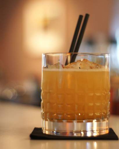 Verre à cocktail avec glaçons et cocktail ambré servi sur ardoise noire, café Honfleur ambiance lounge, restaurant L'Assiette Normande