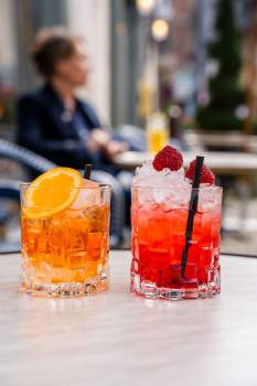 Deux cocktails en verre taillé, un spritz à l'orange et un rouge aux framboises, servis en terrasse café, restaurant L'Assiette Normande à Honfleur