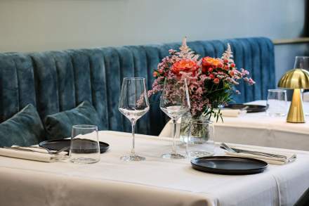 Table dressée avec bouquet de fleurs colorées, assiettes noires et banquette velours bleu, où manger à Honfleur
