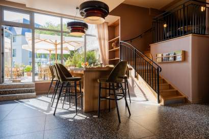 Espace lumineux avec table haute, tabourets noirs et escalier métallique donnant sur jardin, restaurant L'Assiette Normande à Honfleur