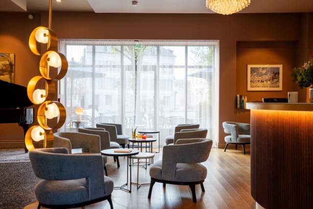 Salon de l'hôtel avec fauteuils bleus et gris, tables basses et grande baie vitrée, hôtel Invitation au Voyage Honfleur