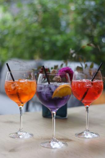 Trois cocktails colorés en verres à pied devant une fenêtre végétalisée, café Honfleur en terrasse, restaurant L'Assiette Normande
