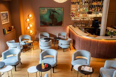 Lounge du bar avec fauteuils gris, tables basses rondes et comptoir rétroéclairé, bar Honfleur en soirée, restaurant L'Assiette Normande